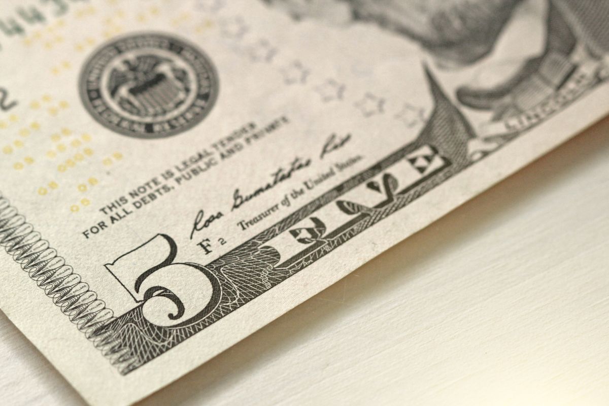 The image tells about a five-dollar bill on the table which means only spending $5 bills is an easy way to build a habit of setting money aside.