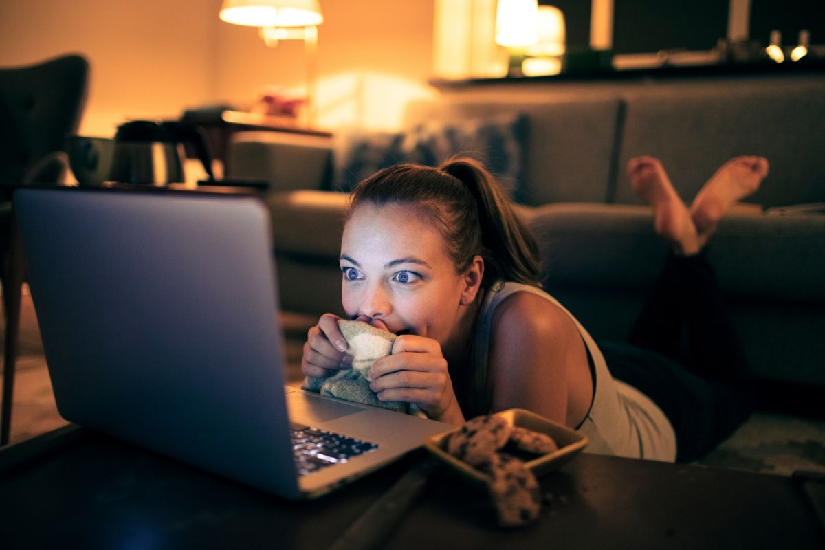 The photo shows a girl watching a movie on the laptop while having a cookie which refers to rewarding yourself from hitting milestones keeps you motivated and builds a savings habit without feeling like you're missing out.