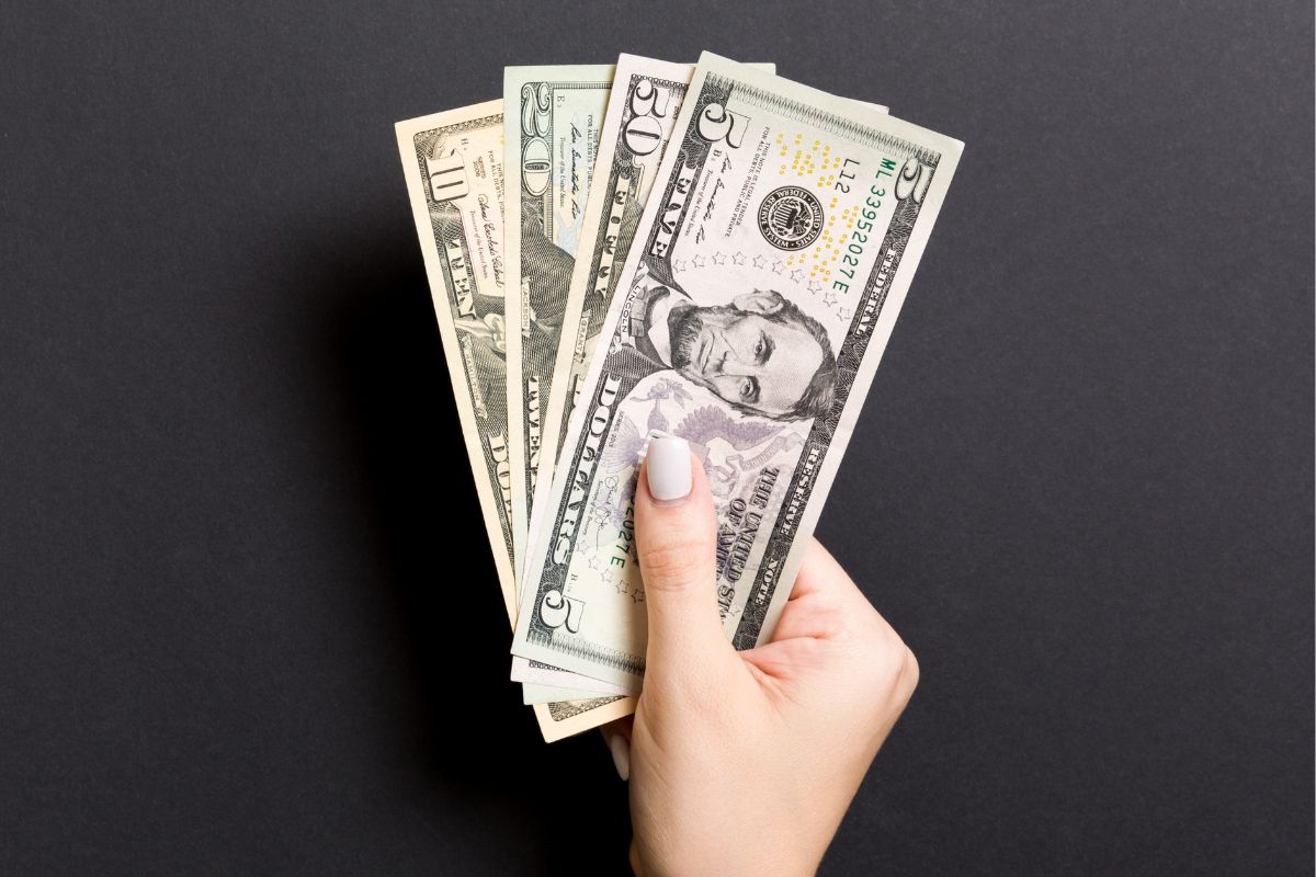 The picture shows a girl's hand holding dollar bills referring to taking the cash-only challenge to help build better money habits while growing your savings.