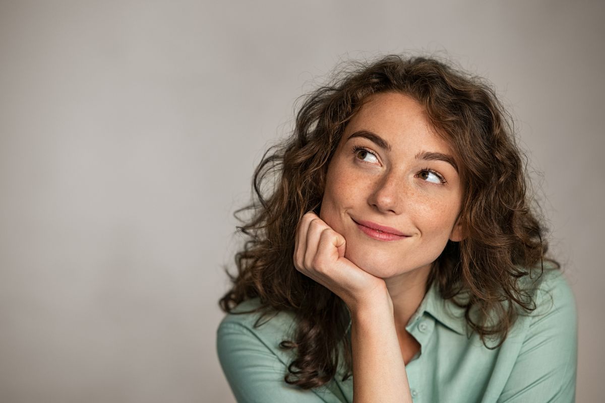 The photo shows a girl thinking while smiling indicating to visualize your future self enjoying the benefits of your savings helps shift focus from short-term wants to long-term benefits.