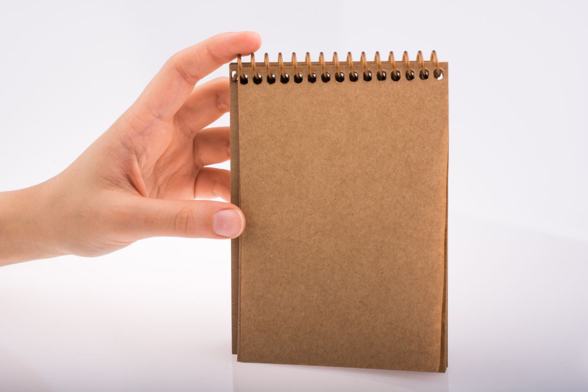 The photo shows a girl's hand holding a notebook referring to keeping a list to see how much you've saved helps curb unnecessary purchases while growing your savings.