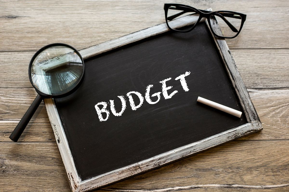 The photo tells about an eyeglass, a magnifying glass, chalk, and a board with a note indicating the use of a reverse budget ensuring savings are a priority rather than an afterthought.