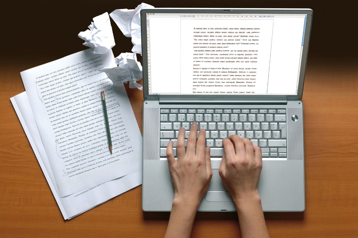 The image tells about papers, crumpled papers, a pen, and a girl's hand typing on the laptop which means offering freelance services can start with little experience by taking small gigs to build your reputation.