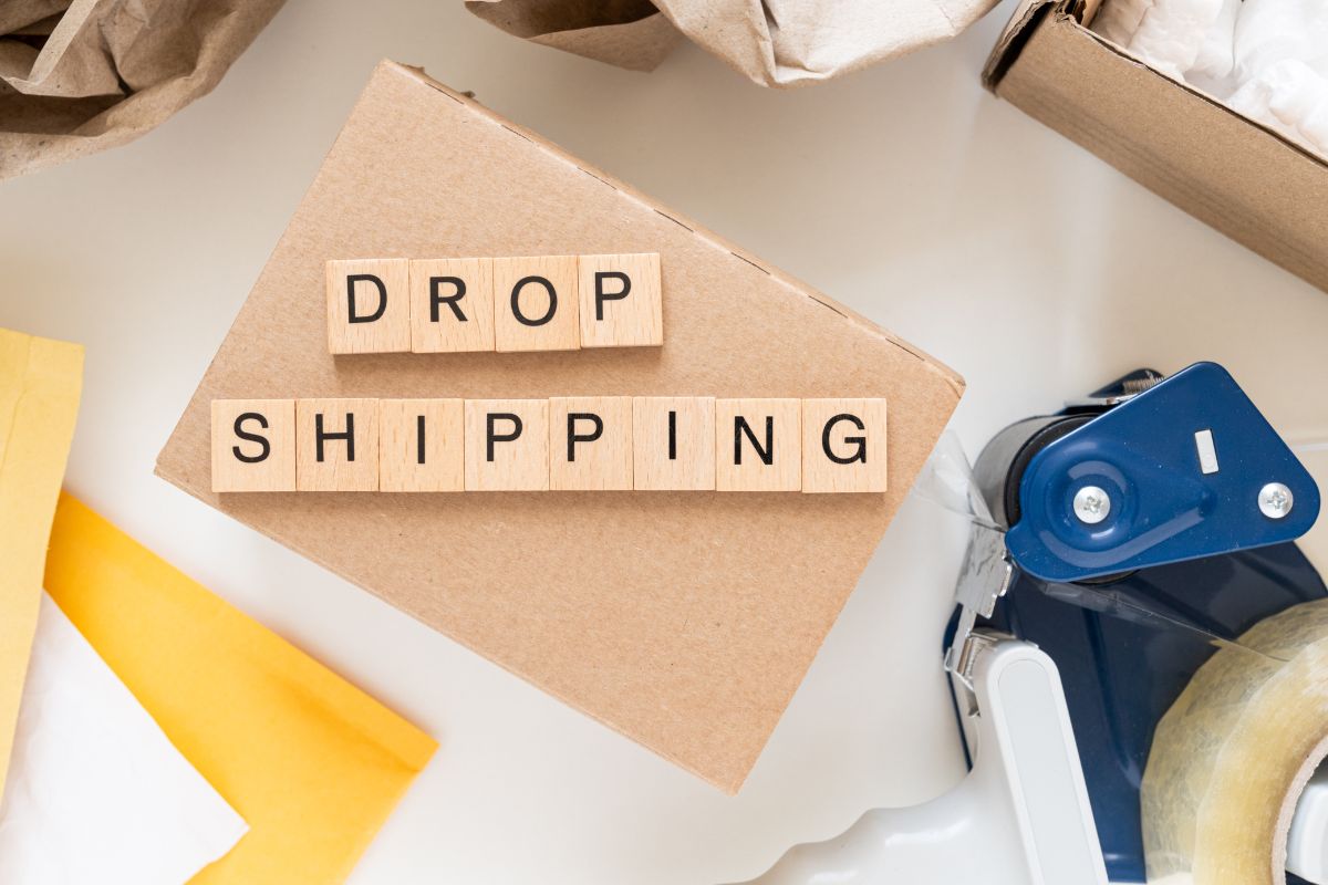 The photo shows boxes, tape, and wooden cubes with letters indicating that starting a Dropshipping store with no inventory is a popular beginner-friendly online business.