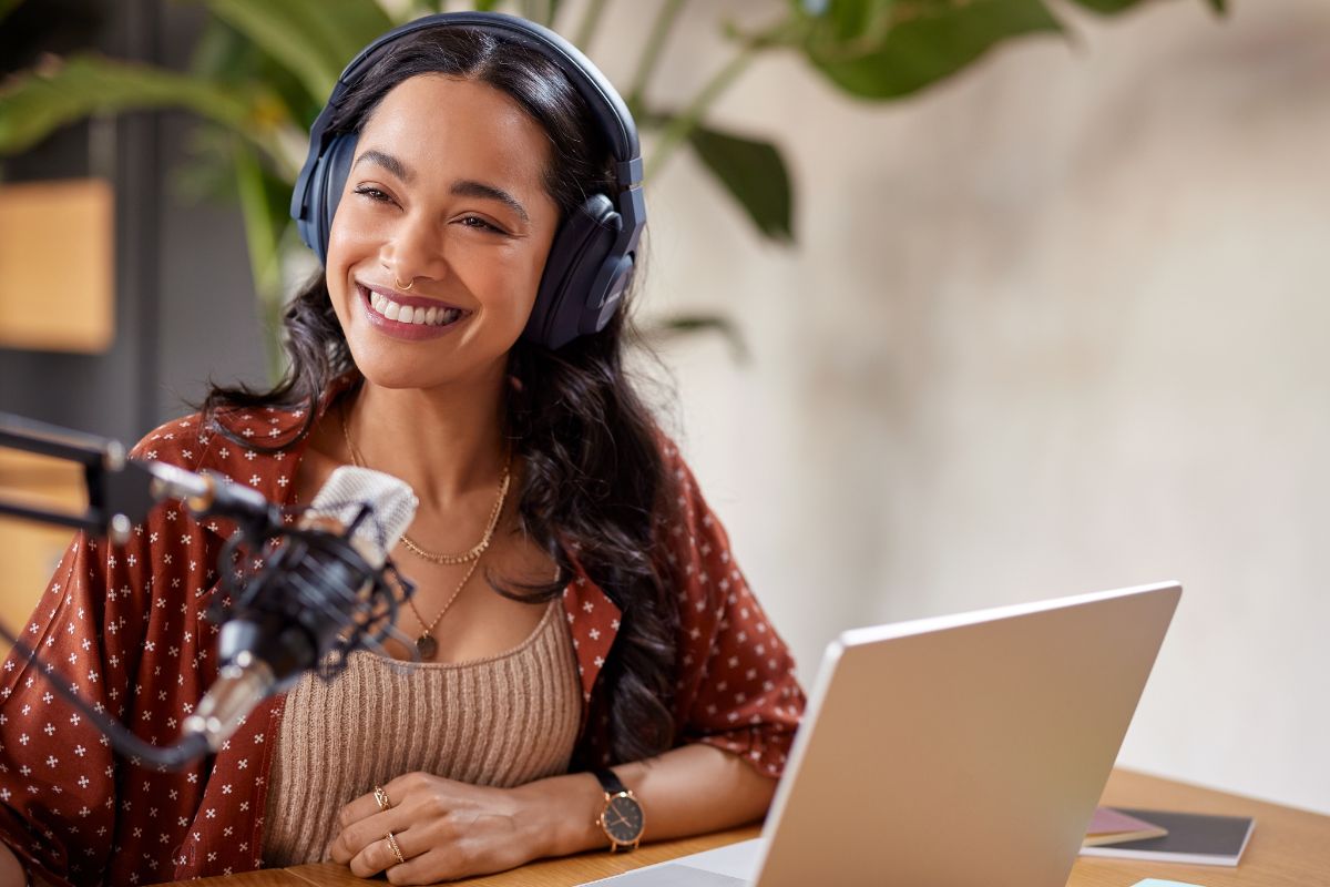 The picture shows a laptop and a girl using a headphone while recording on the microphone indicating that starting a podcast and monetizing with sponsorships is beginner-friendly because you don't need fancy equipment to get started.
