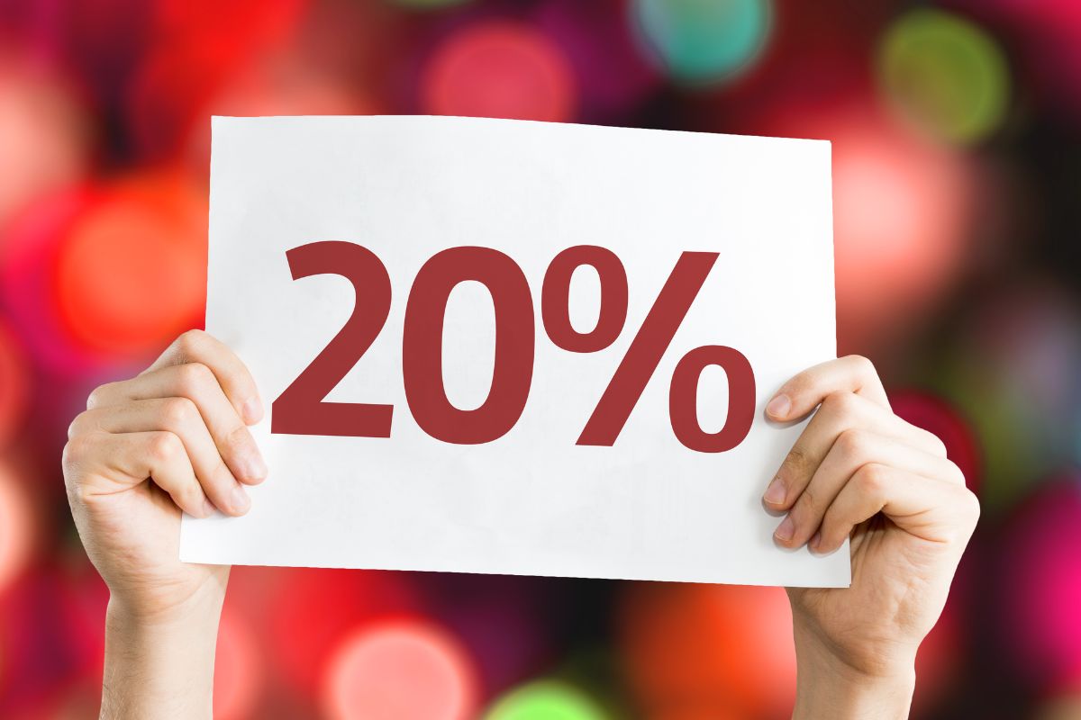 The image shows a girl's hand holding a piece of paper with a number and percentage which means 20% should go to savings and debt payments to help create a safety net and build wealth over time.