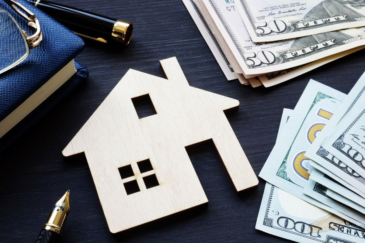 The picture shows dollar bills, a pen, a notebook, and a mini house figure referring to housing as the most important part of any budget that helps you avoid stress and late payments.