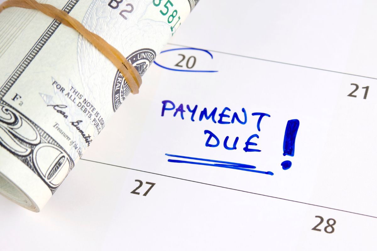 The photo shows a calendar with notes and rolled dollar bills indicating that debt payments should be a priority in your budget to help you avoid late fees and financial stress.