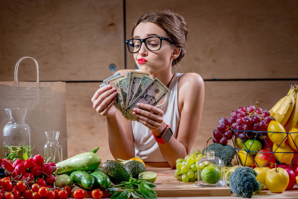 The image tells about fruits, vegetables, a paper bag, and a girl counting dollar bills indicating that food should always be a key part of your budget and plan to avoid overspending.