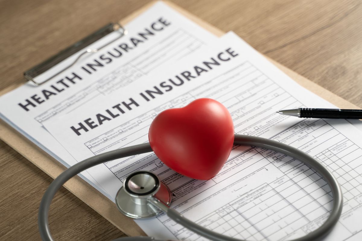 The picture tells about a pen, a stethoscope, a heart shape, and a clipboard with papers referring to insurance and healthcare costs to help you avoid financial trouble when unexpected health issues come up.