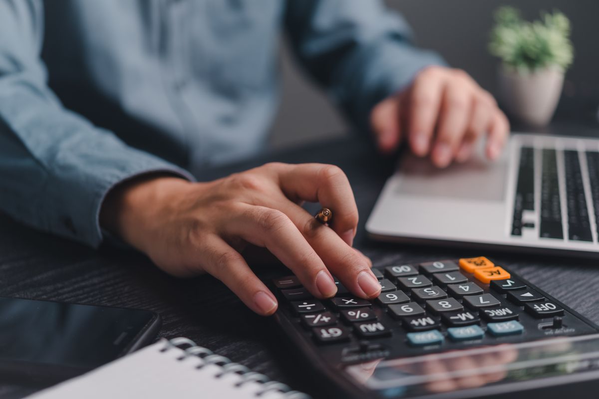 The photo tells about a notebook, a laptop, and a man calculating referring to check out the over 100 budgeting categories to make sure every dollar is accounted for.