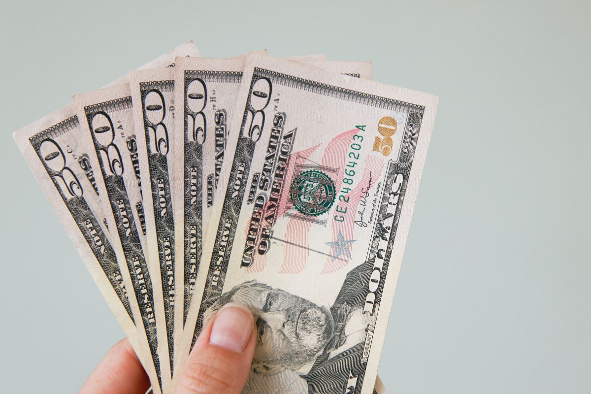The photo tells about a girl's hand holding dollar bills which means using the invisible money trick to grow your savings without feeling like you're making a sacrifice.