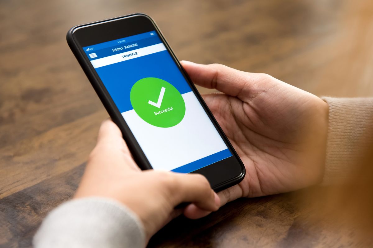 The picture of a girl's hand holding a phone with a screen display referring to an automated transfer to savings before paying any bills helps you stay on track and reach your goals faster.