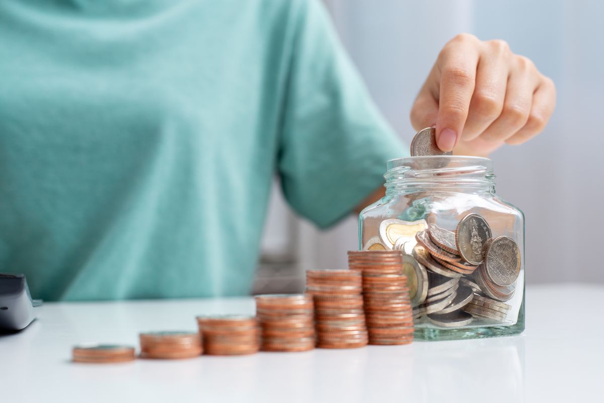 The photo shows coin stocks and a girl's hand putting coins into a jar which refers to setting ridiculous and exaggerated savings goals that keep you focused and make savings a game instead of a chore.