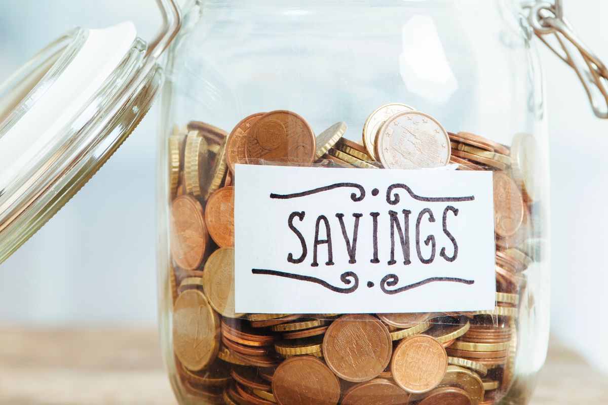 The photo tells about a jar filled with coins and with a note which means to treat savings like a non-negotiate bill keeps you from making excuses and helps you build wealth over time.