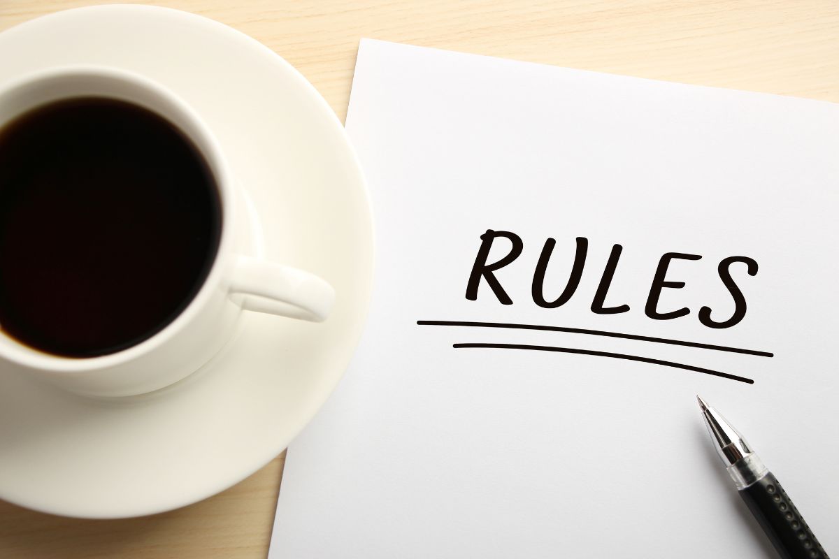 The photo shows a coffee, a pen, and a piece of paper with notes which means that defining clear rules helps you stay on track and reach your money-saving goals.