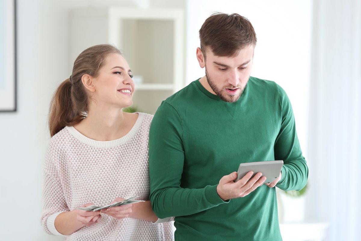 The photo shows a man calculating and a girl holding dollar bills indicating that a spending buddy can help talk through temptations and celebrate wins.