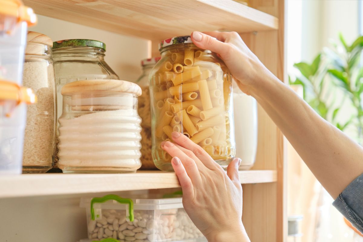 The photo tells about different kinds of ingredients on the container and a girl's hand getting the pasta container referring to meal prep using only the pantry to avoid grocery runs that help stretch what's on hand and keep spending in check.