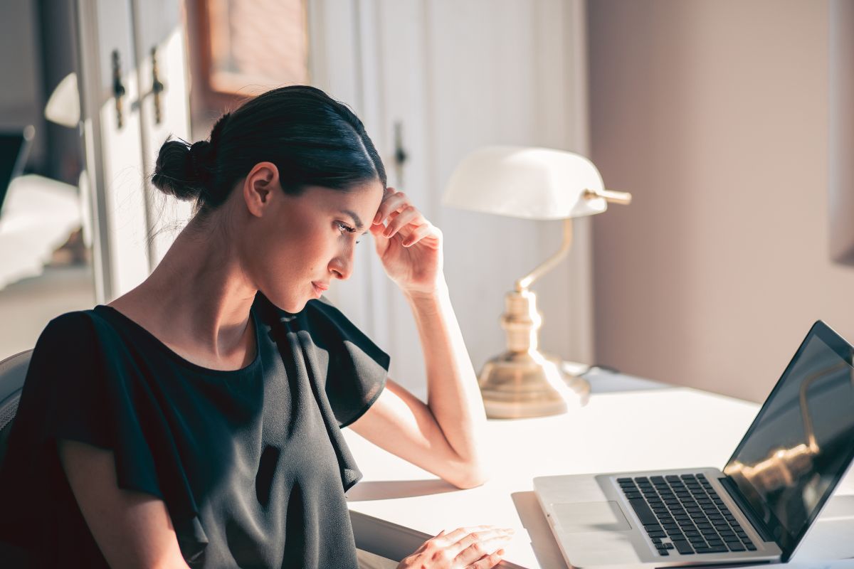 The photo tells about a girl thinking while looking at her laptop indicating to imagine losing your income and asking yourself if you'd still buy if your paycheck stopped tomorrow, helps you focus on essentials and build better financial habits.