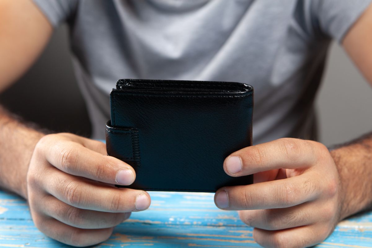 The image shows a man holding a wallet which refers to trying a no-buy year for wants to help break the habit of spending on non-essentials.