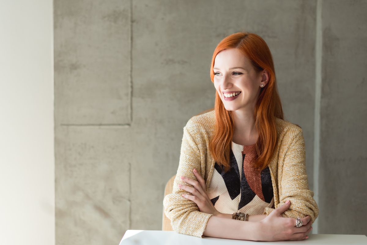 The image shows a girl smiling while sitting indicating that motivation to stay on track gets, avoid unnecessary spending gets easier when you focus on long-term goals.