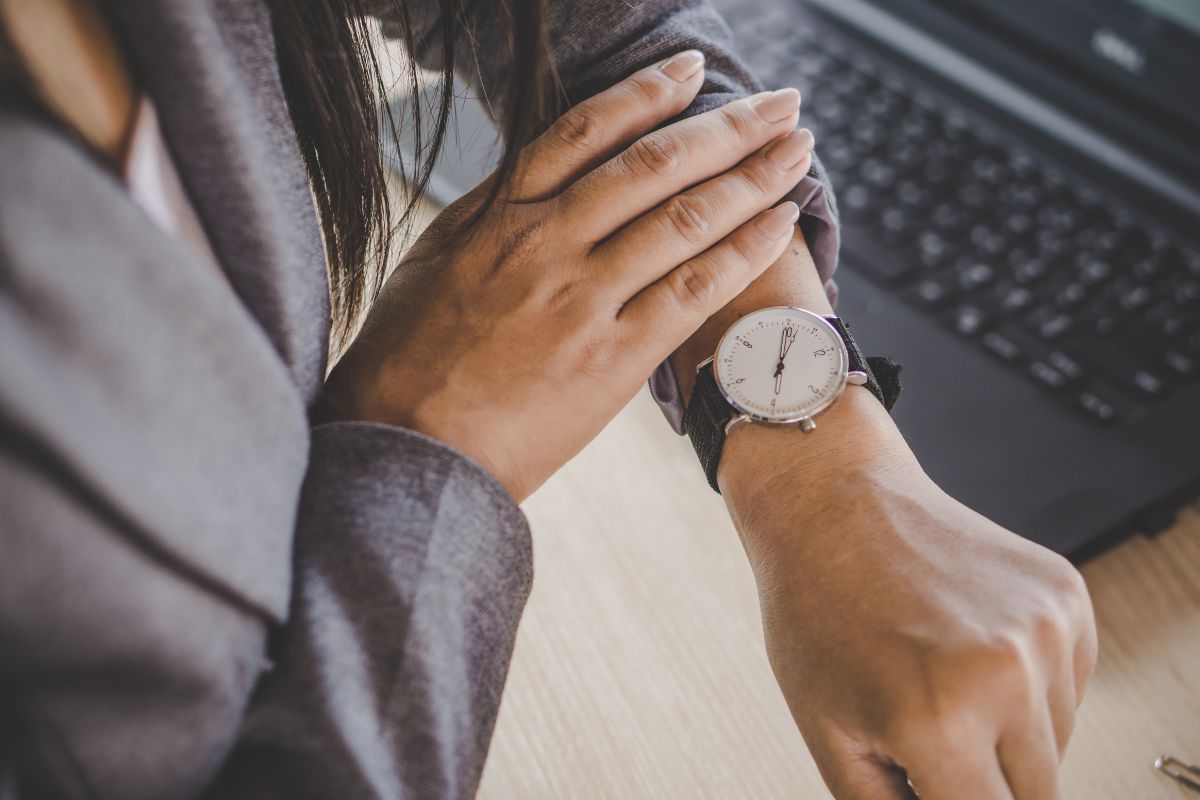 The image tells about a laptop and a girl's hand checking her watch referring to challenging yourself to go longer helps break spending habits and keeps more money in your pocket.