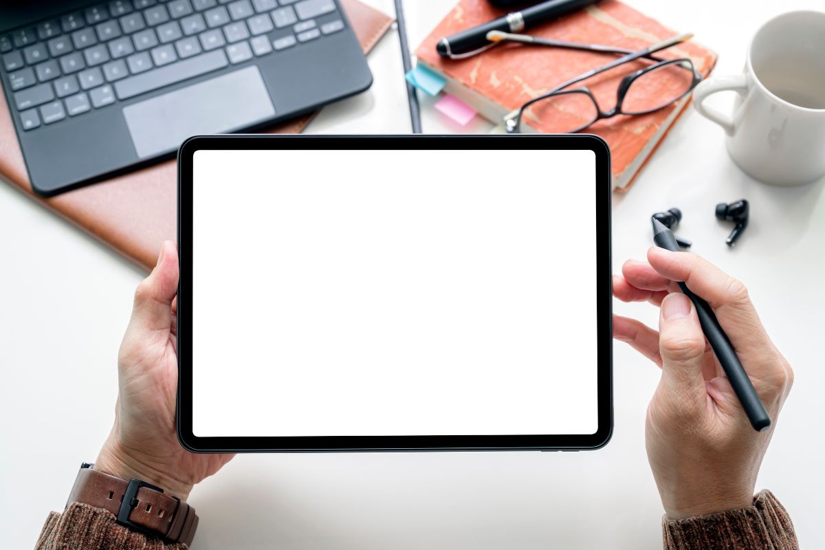 The image shows a keyboard, an eyeglass, a notebook, a pen, a mug, and a girl's hand holding a pen and a tablet which means tracking progress with Apps helps you see where you can do better.