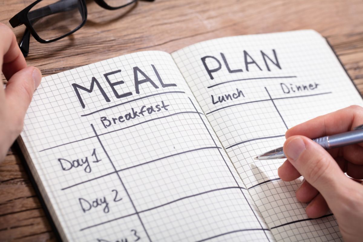 The picture shows an eyeglass and a man's hand and writing on the notebook indicating that meal planning using the existing pantry saves money and reduces waste.