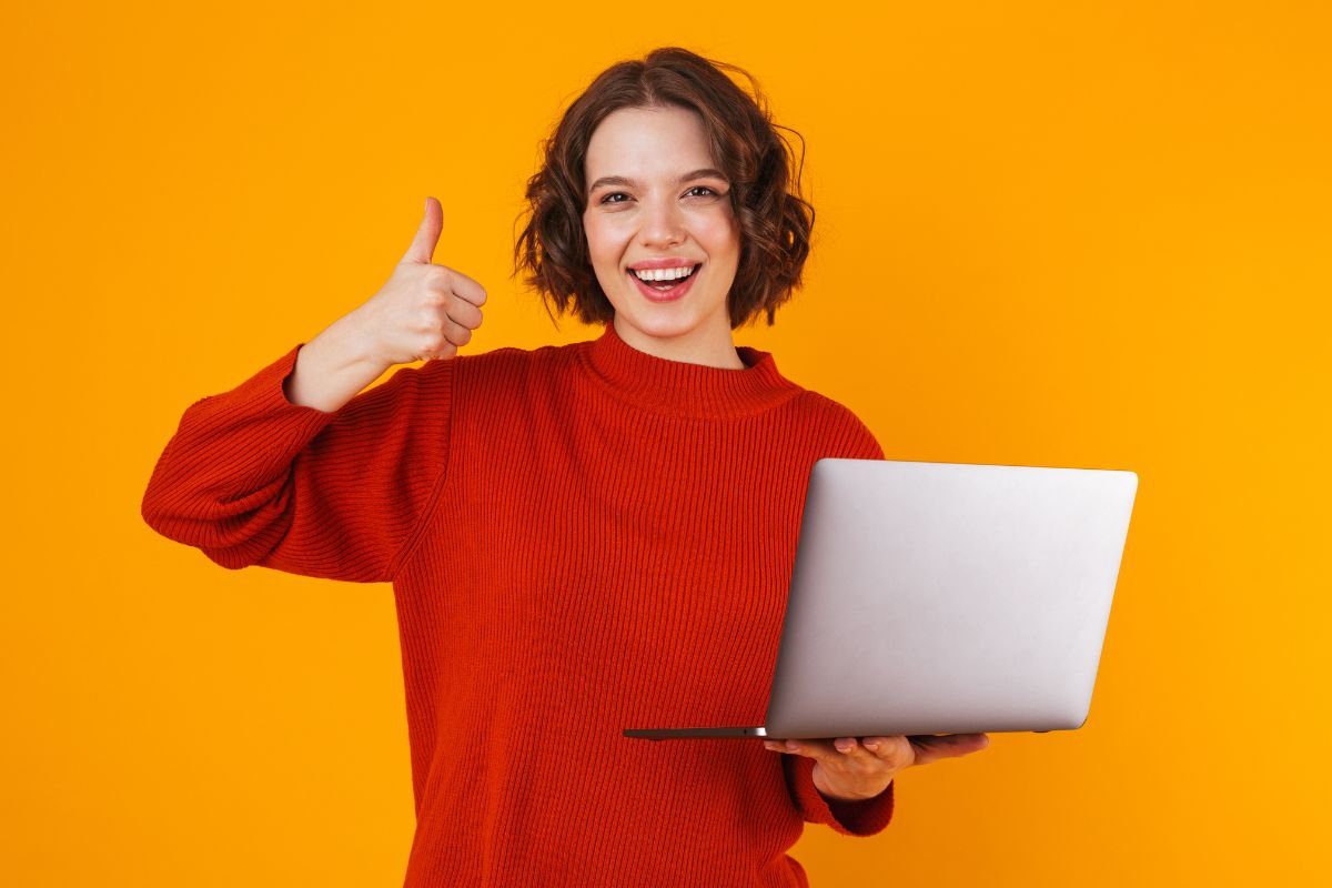 The photo shows a girl holding a laptop while doing an ok sign referring to learning to live within your means gives you more control over your future.