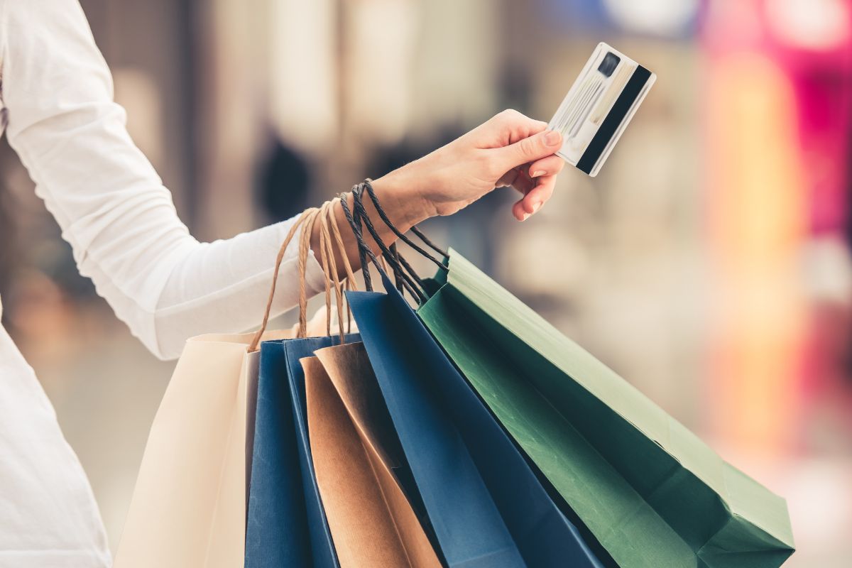 The photo tells about a girl carrying shopping bags and holding a credit card referring to avoiding lifestyle inflation, which helps build wealth faster and reach financial freedom.