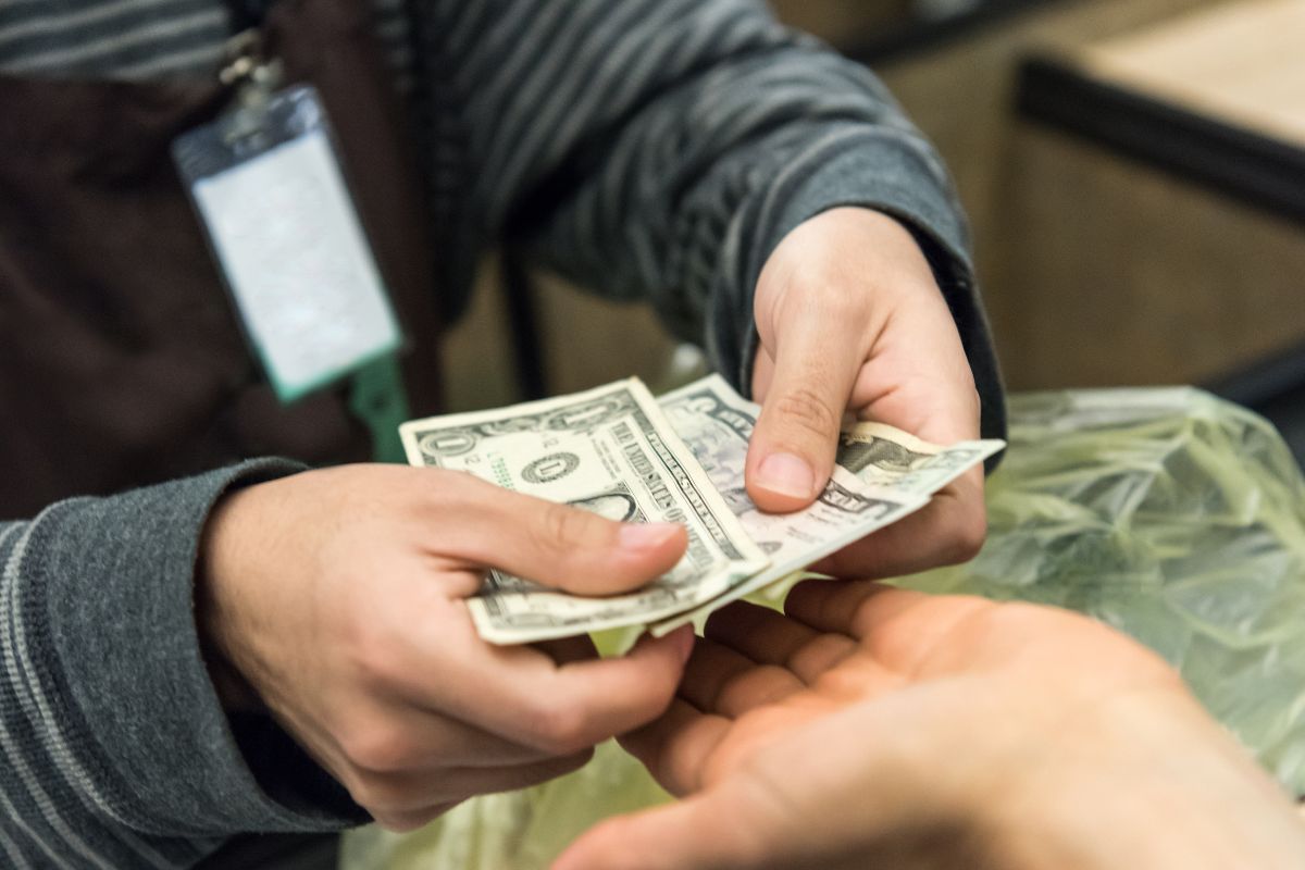 The picture tells about a cashier's hand giving the dollar bill change to the customer's hand which means using cash instead of credit helps you stay within your budget and avoid financial stress.