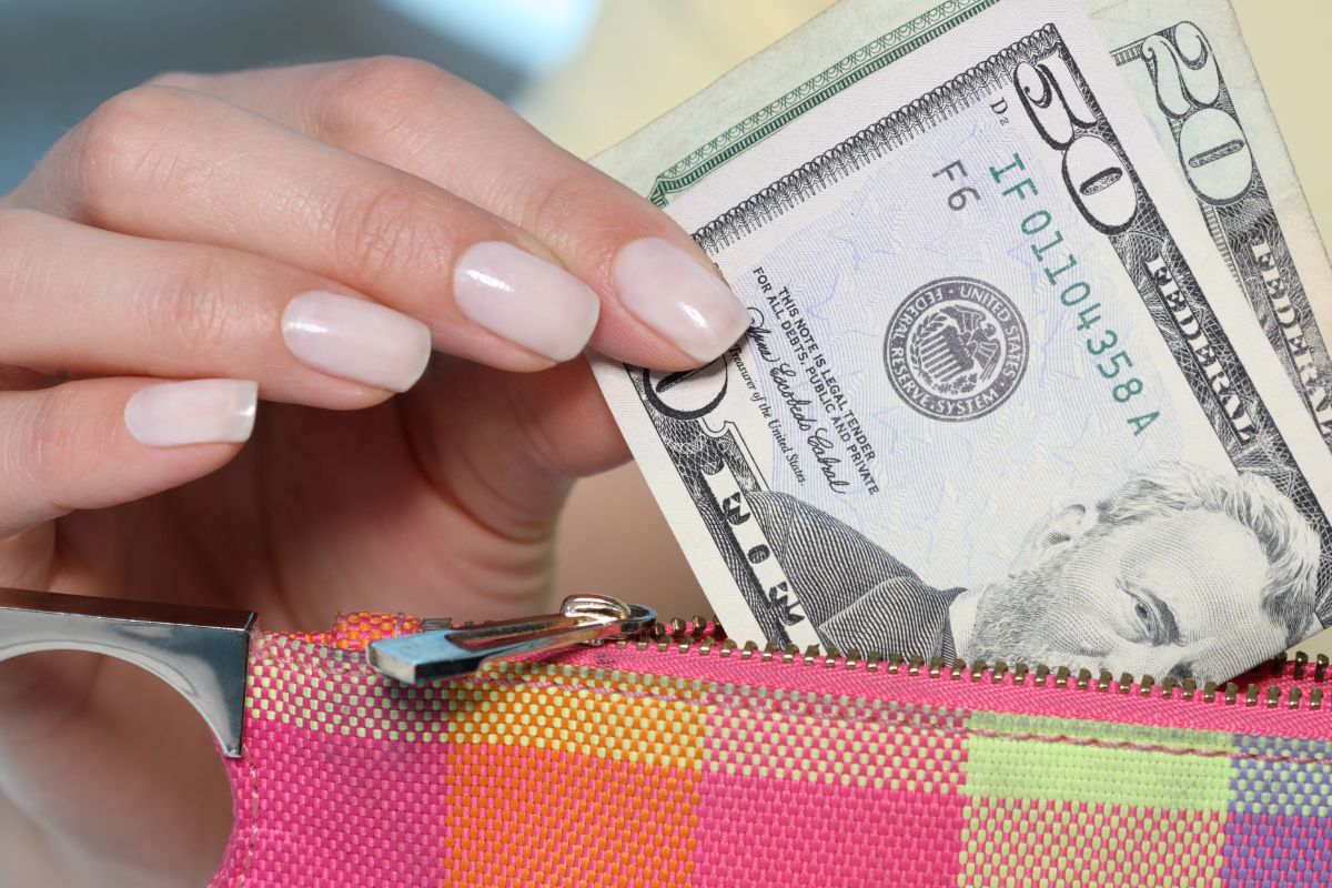 The photo of a girl's hand pulling out dollar bills inside her wallet refers to reflects on spending habits and helps you adjust your future budget and build money spending habits.
