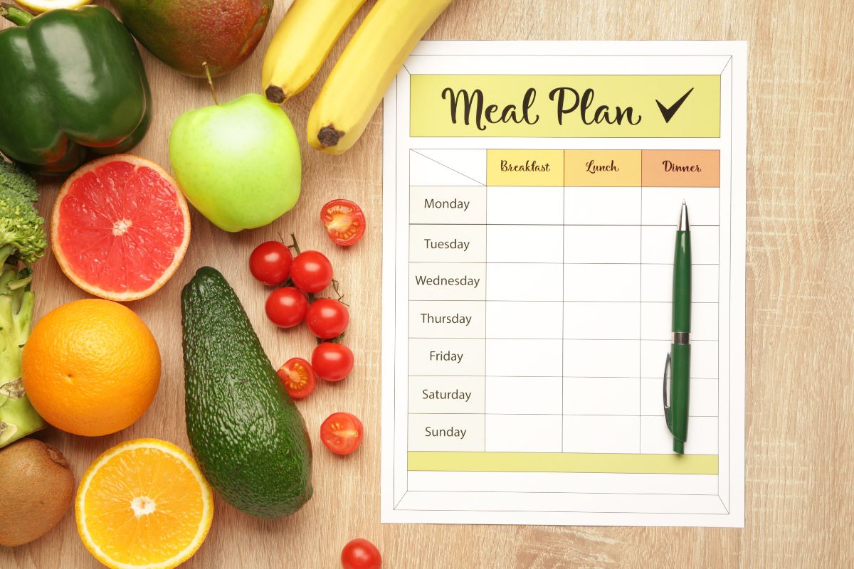 The photo shows fruits, a pen, and a piece of paper with notes referring to meal plans and cooking at home helps avoid last-minute takeout and makes it easier to put more money toward savings.