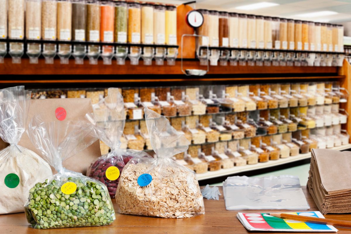 The image shows spices on the containers, beans, oats, paper bags, plastics, and pens on the table which means buying in bulk for essentials helps reduce your total spending and keeps extra cash in your pocket.