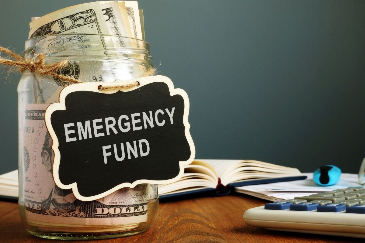 The image shows a calculator, a notebook, and a jar filled with dollar bills and notes referring to building and maintaining an emergency fund to prevent small setbacks from turning into big financial problems.
