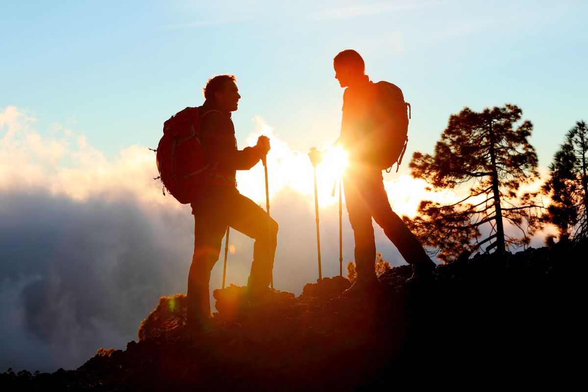The image tells about two people holding sticks and carrying backpacks at the mountain which means to go for a hike is an easy way to have fun without spending money.