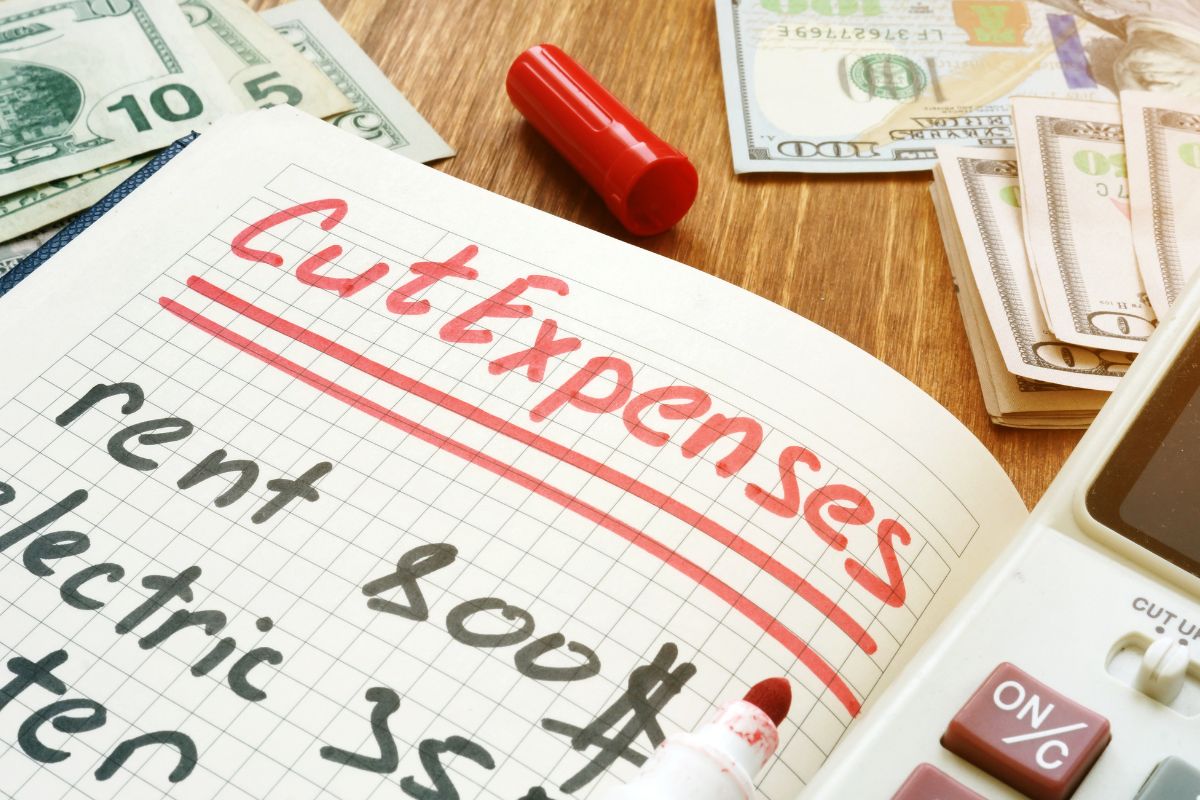 The picture shows money and a notebook with cut expenses wording.