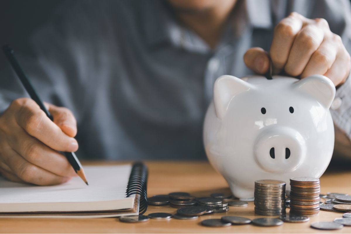 The picture shows a man saving money while writing on the paper.