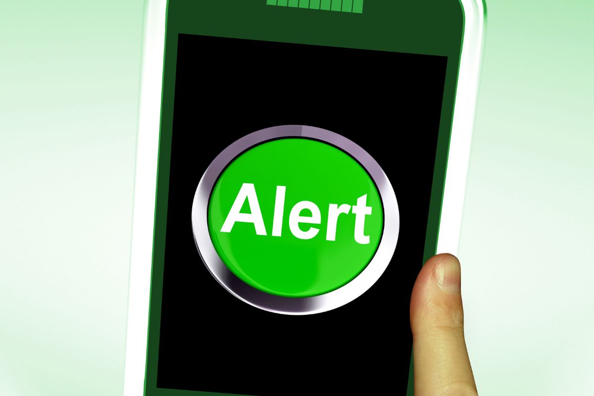 The picture shows a man's hand holding a phone with an alert display.