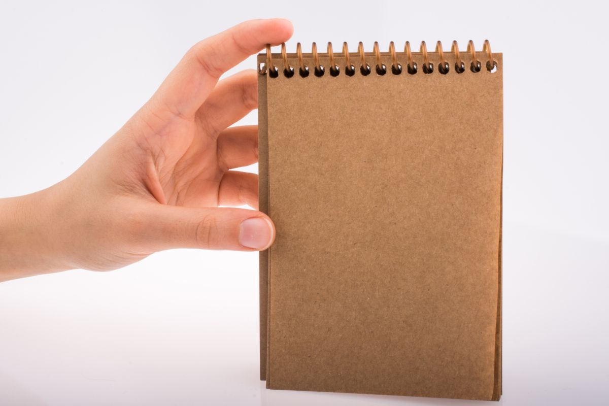 The photo shows a woman's hand holding a notebook.