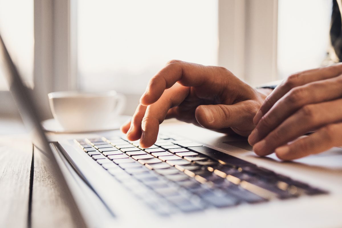 The image shows a man's hand typing on his laptop.