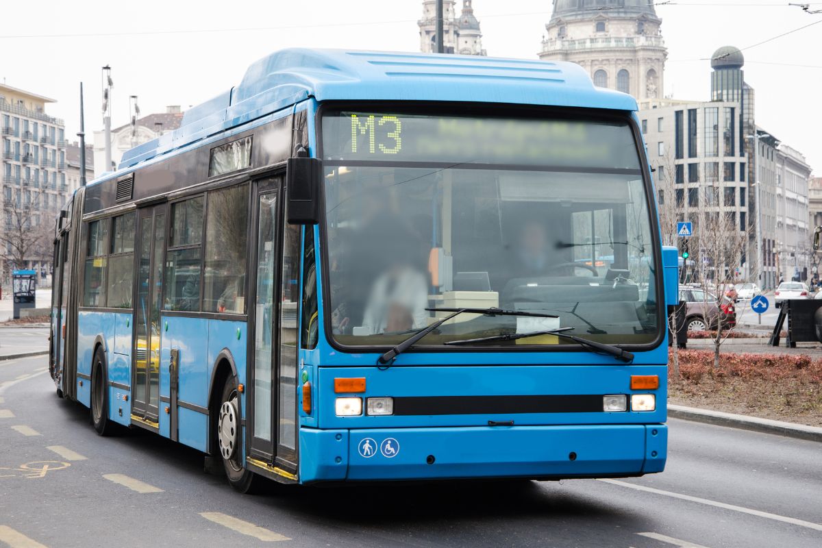 The image shows a bus on the road city indicating to use public transportation helps leave more room in the budget for savings.
