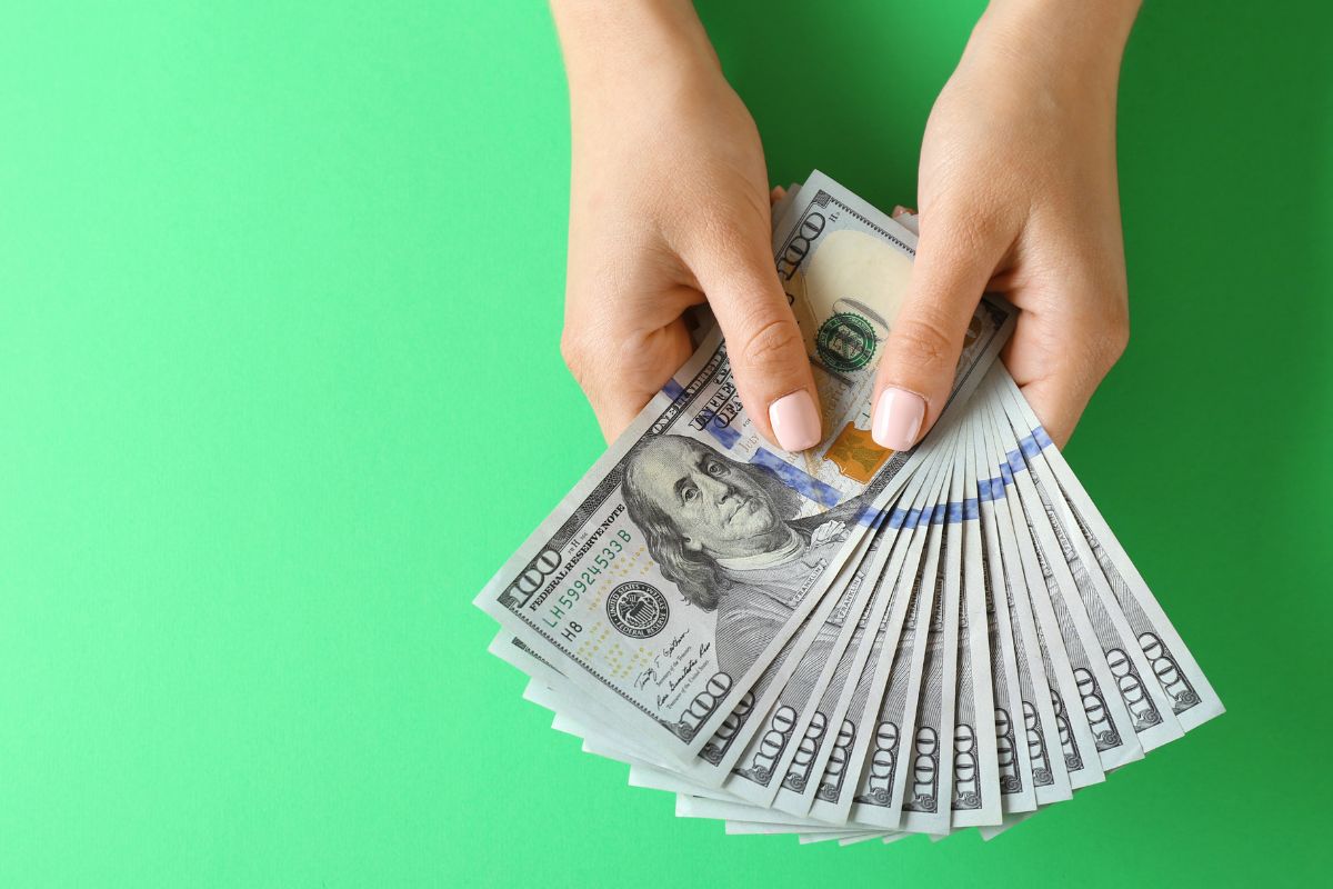 The picture tells about a girl's hand holding a dollar bill referring to the focus on financial moves that keeps you on track and is the key to building long-term wealth.