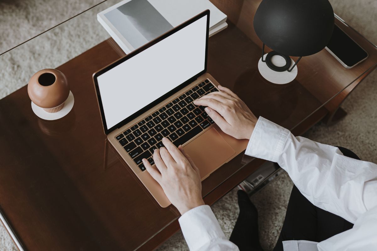 The image tells about lamps, books, a phone, and a man's hand typing on the laptop indicating that learning how to become the next millionaire with no money helps create financial security.