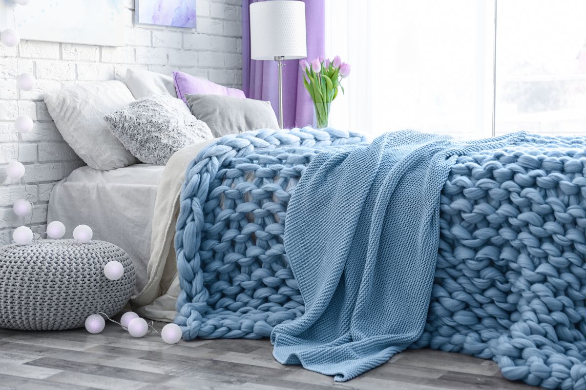 The picture tells about a cozy bed with pillows, a lamp, and blankets, indicating that rearranging a room using what you have is a productive way to refresh your space without spending money.