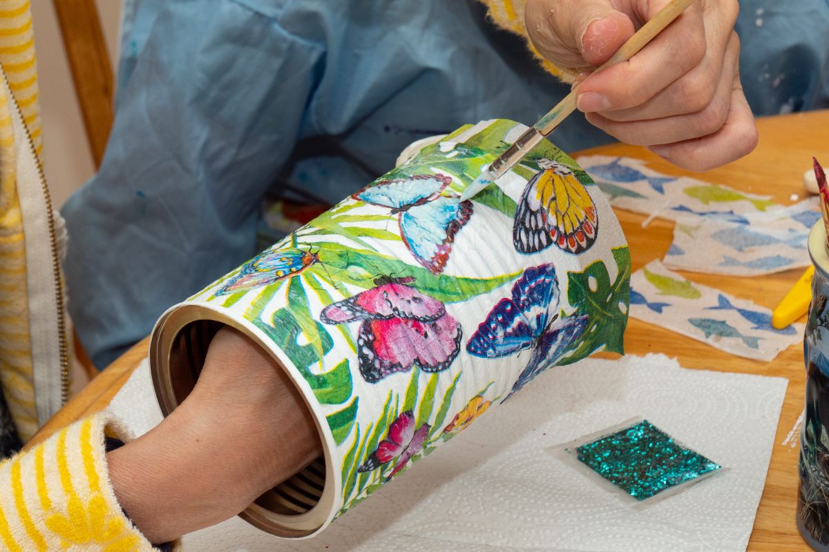 The photo shows glitter and a girl's hand painting the can indicating that trying a new craft is a fun way to pass time without spending money.