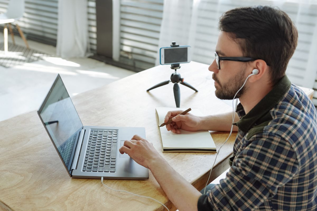 The image shows a tripod with a phone and a girl using a laptop while taking notes referring to learning a new skill with free online tutorials as a productive way to use your time while voiding unnecessary spending.
