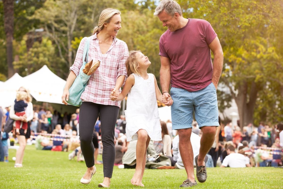 The image shows a group of family at the park with the people around which refers to attending a free local event as a great way to get out of the house and find new experiences.