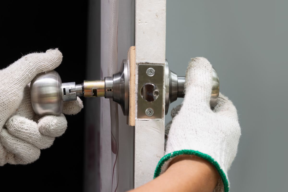 The picture of a man's hand fixing a door knob.