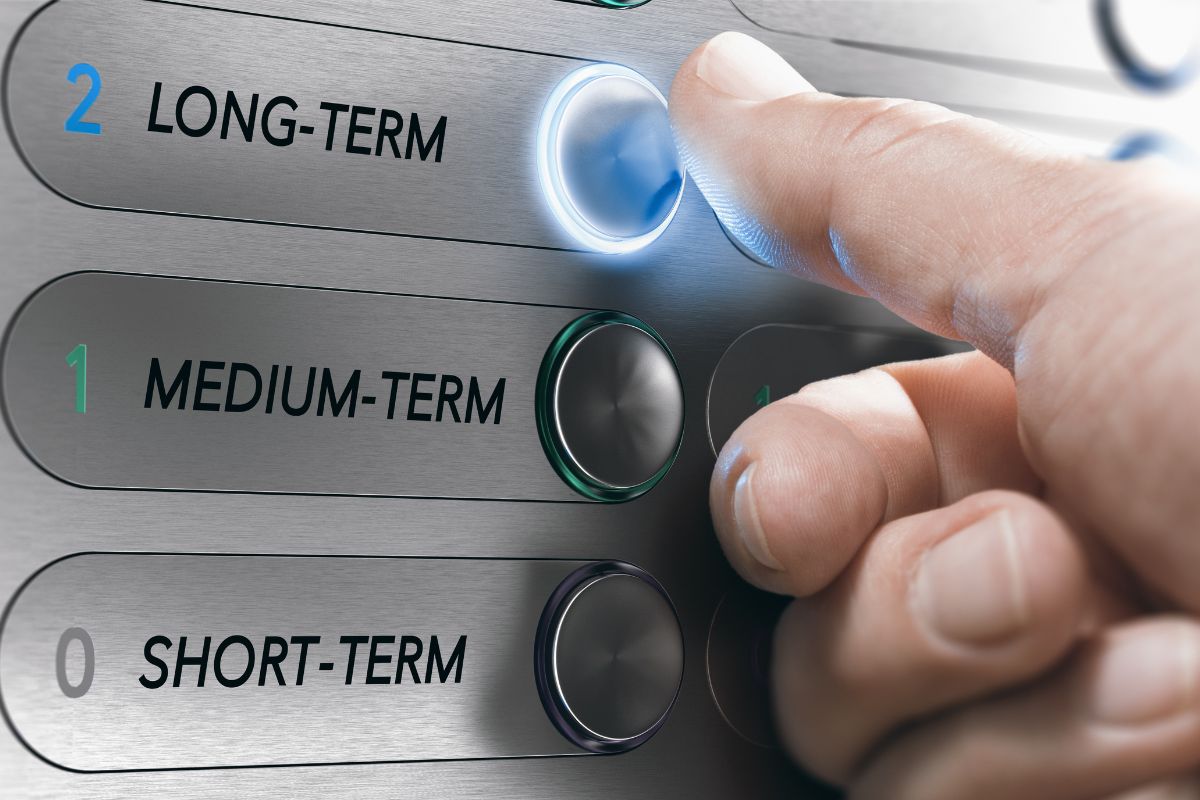 The image shows a man's hand pressing the first button to prioritize long-term gains and build lasting wealth.